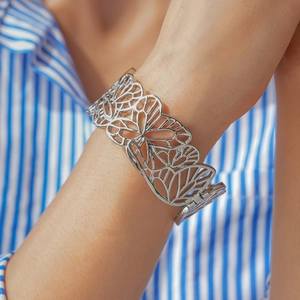 Détail d'un bracelet manchette papillon argenté porté sur une manche de chemise rayée