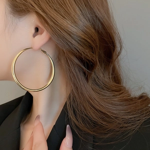 Close-up of model wearing large minimalist golden hoop earrings with shiny finish