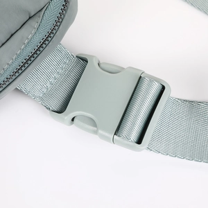 Detail view of the durable plastic buckle and nylon strap on a gray-green crossbody bag