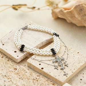 Detail of double-layer pearl necklace with rhinestone cross pendants on stone surface