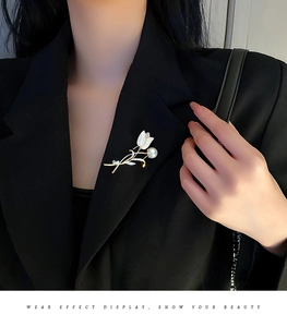 Détail d'une élégante broche tulipe dorée avec perles et cristaux sur une veste noire