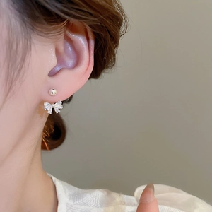 Close-up of silver bow earrings with zircon stones worn by a model on a grey background