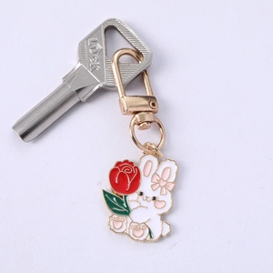 Detail of a white enamel rabbit keychain holding a red rose with golden metal finish