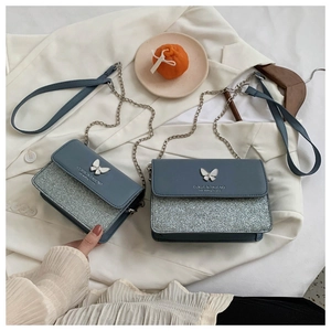 Detailed view of greyish-blue crossbody bag with white butterfly buckle and silver sequins