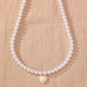 Detail of white pearl necklace featuring a gold-edged heart pendant on beige linen fabric