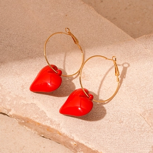 Detail of elegant gold hoop earrings with glossy red resin heart charms on stone base