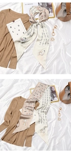 Detail of a beige silk twilly scarf with cartoon cat print tied in a bow on a white background