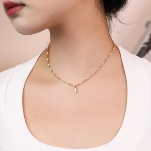 Detail of gold cross necklace with white enamel beads worn on a neck for elegant style
