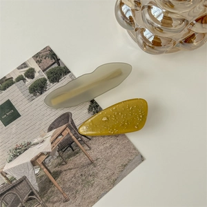Close-up of wavy green and amber acetate hair clips with gold leaf flakes detail