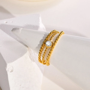 Goldener dreilagiger Kordelring mit zentralem Zirkonia auf einem weißen Display-Ständer