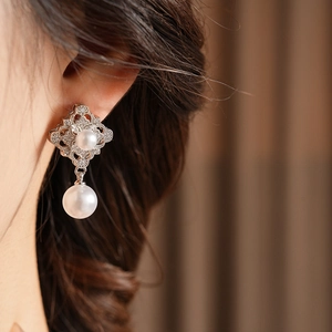 Detailed close-up of a vintage hollow diamond and pearl drop earring on model