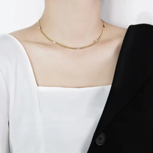 Detail of a thin gold snake chain necklace with rectangular zircons on a model's neck
