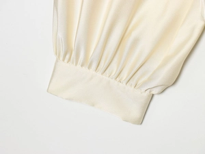 Gros plan détaillé des poignets de chemisier en satin jaune crème avec plis élégants