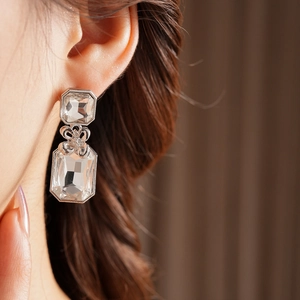 Close-up of square crystal drop earrings with decorative silver bow on model ear