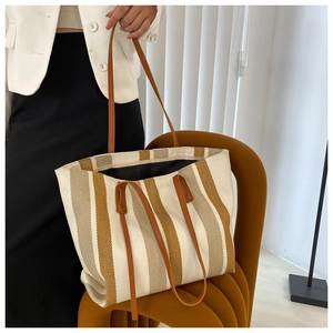 Detail of canvas tote bag showing vertical stripes, leather handles and zipper closure
