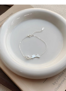 Vista macro del bracciale in argento S925 con charm a gatto e perla su piatto bianco