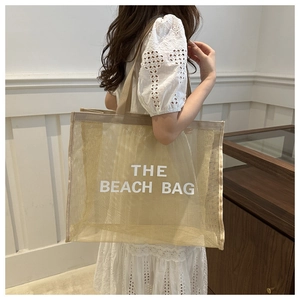Detail of khaki mesh beach bag with THE BEACH BAG logo shown on model shoulder