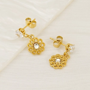 Detail of gold petal-shaped drop earrings with clear zircon stones on a ceramic plate
