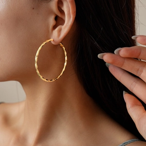 Detail shot of a model wearing a twisted 14k gold plated geometric hoop earring