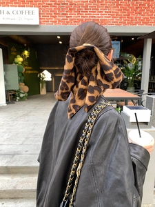 Close-up of a leopard print silk hair scarf styled on a bun against a brick wall background