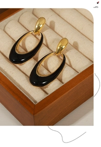 Close-up of gold oval enamel earrings displayed in a luxury wooden jewelry box