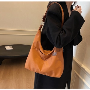 Detail view of an orange nylon tote bag worn by a model in a minimalist indoor setting