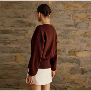 Detail of burgundy ribbed knit cardigan hem with a long sleeve design on a model