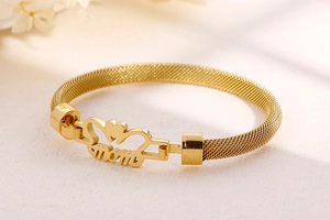Close-up of golden mesh bracelet with MOM lettering and heart pendant detail