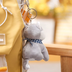 Detail of grey husky plush keychain with blue scarf hanging on a yellow backpack