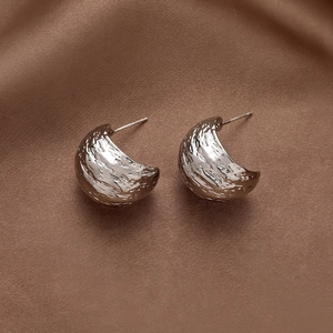 Hammered texture silver C-shape earrings on brown satin fabric background