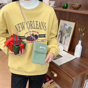 Detail of green plush mini crossbody phone bag with flap and purple strap on yellow hoodie
