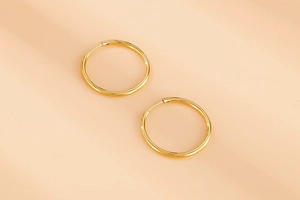 Macro detail of polished gold-plated stainless steel hoop earrings on warm beige background