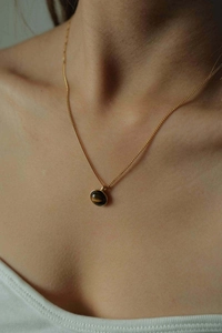 Detail of 18K gold necklace with oval tiger eye pendant on model collarbone