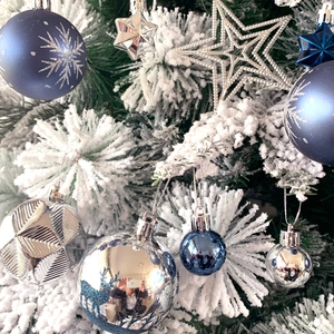 Close-up of blue and silver Christmas tree ornaments with snowflakes on snowy branches