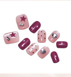 Close-up of pink cat eye press-on nails with red stars, black dots, and 3D heart rhinestones