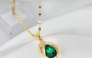 Detailed close-up of a gold teardrop pendant with a green gemstone on white silk