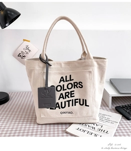 Detail of minimalist canvas tote bag featuring front pocket and printed slogan for daily use