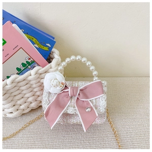 Close-up of pink tweed child handbag with pearl handle, bow, and camellia charms