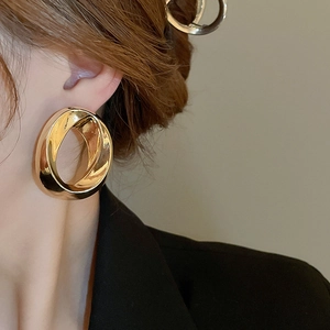 Close-up of a model wearing chunky gold hollow oval earrings with a twisted metal texture