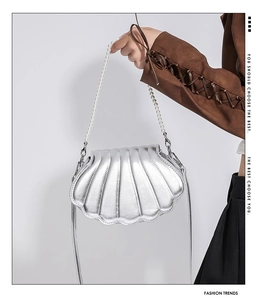 Silberne Handtasche in Muschelform mit Perlengriff und Metallic-Textur von Model gehalten
