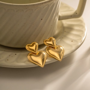 Detailed view of gold double heart stud earrings resting on a white ceramic teacup