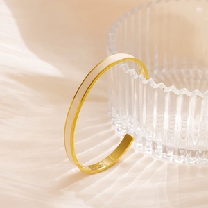 Nahaufnahme eines goldenen C-Armreifs mit weißem Emaille auf einem strukturierten Glas