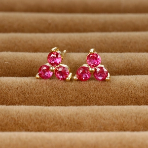 Macro view of gold clover stud earrings with three red round-cut gemstones in prong setting