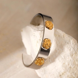 Minimalist silver stainless steel open bangle with golden flower accents on a stone