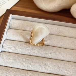 Détail macro d'une bague dorée minimaliste sertie d'une grande pierre en résine laiteuse