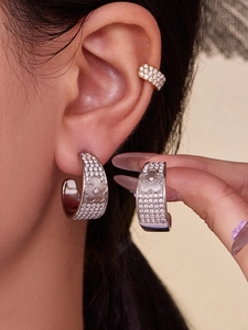 Macro detail of vintage-style C-shaped silver earrings with zircon inlay on model's ear