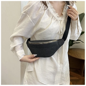Detailed shot of a black canvas crossbody waist bag with gold zipper on a model