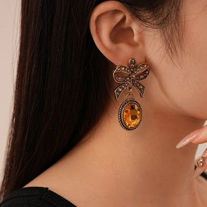 Close-up of vintage bow earrings with oval amber stones worn by a model in warm light
