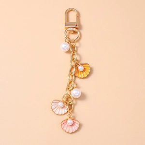 Detailed close-up of golden keychain with pink and yellow enamel shells and round pearls