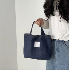 Detail view of deep blue denim tote bag featuring a cute white bear patch on the front